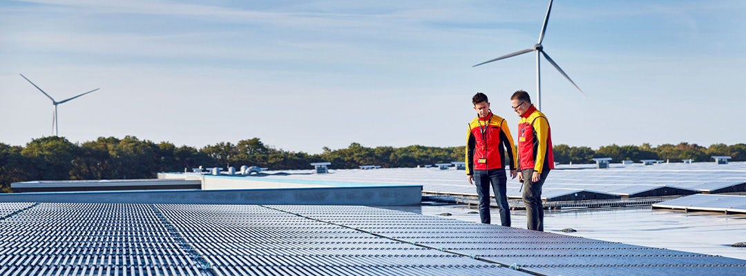 two men in DHL uniforms standing in front of solar panels