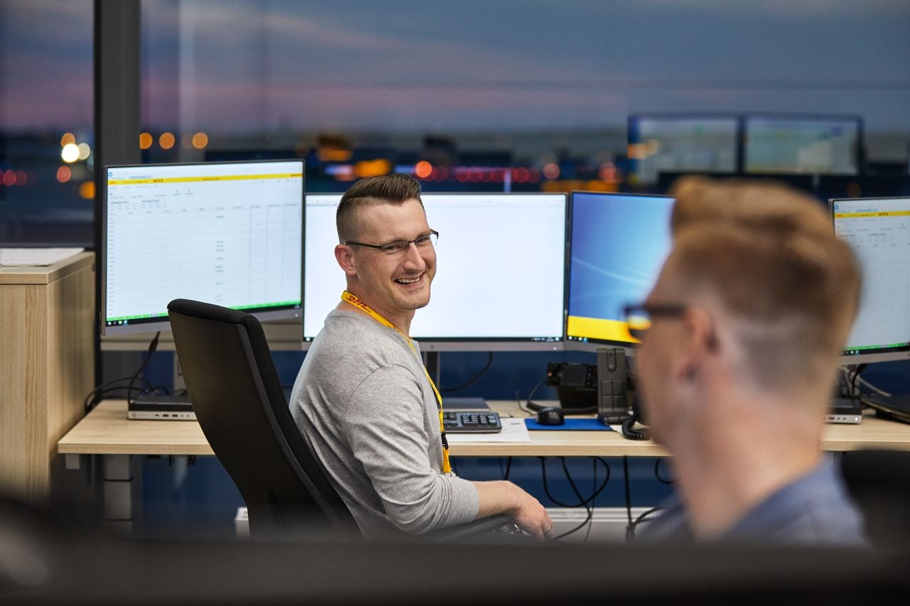 Two DHL employees talk in office sitting at their desk