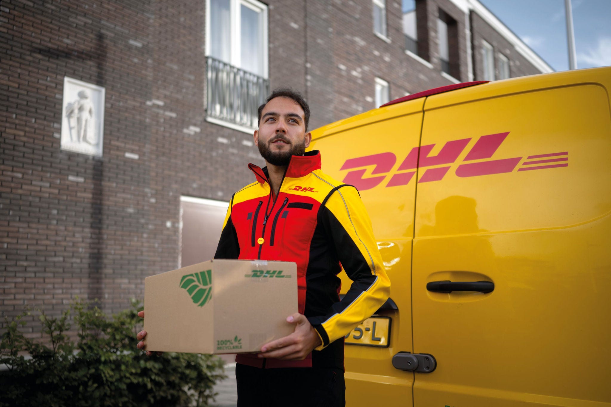 dhl express courier carrying a parcel out of his van