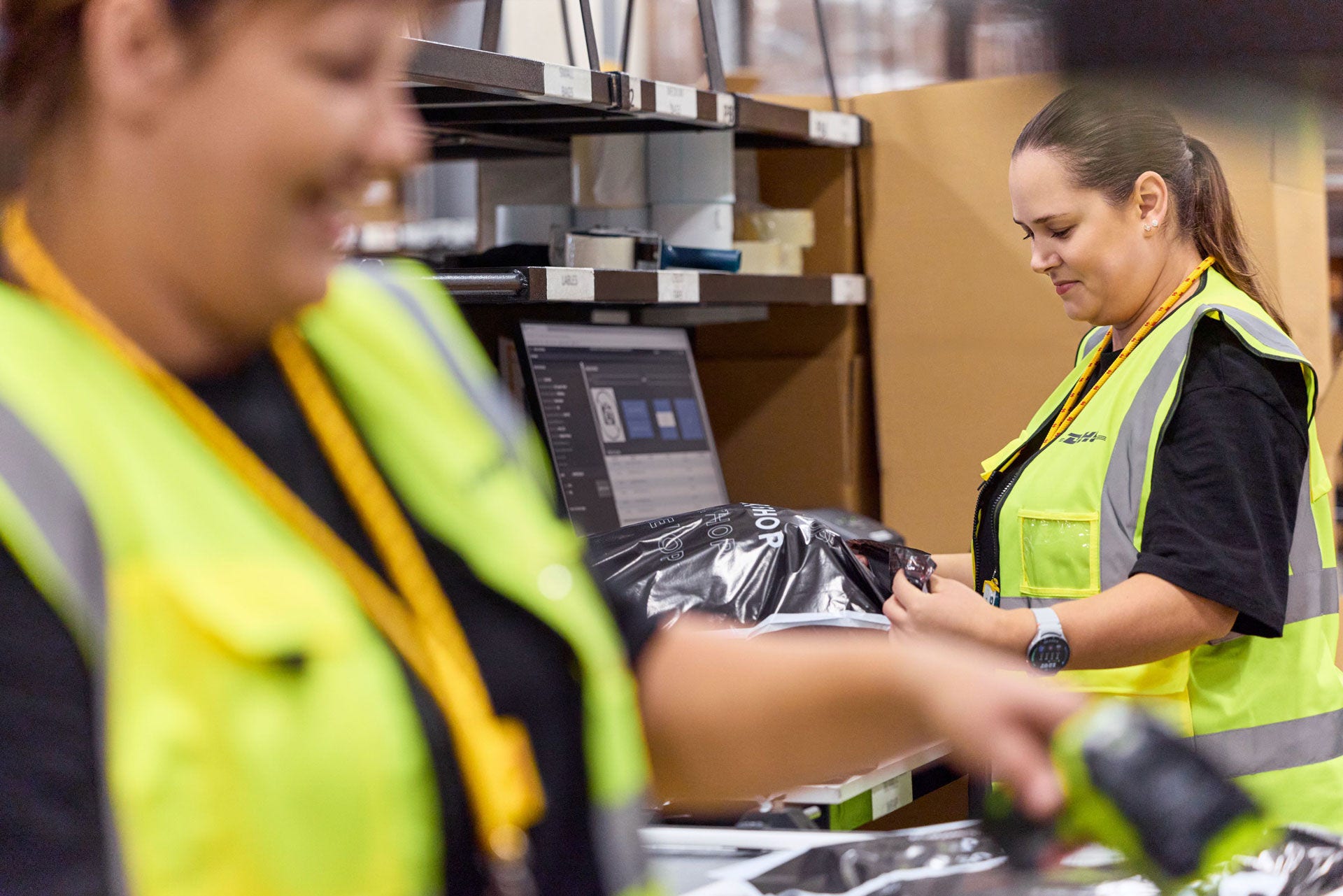 Two female DHL employees are packing parcels in a warehouse.