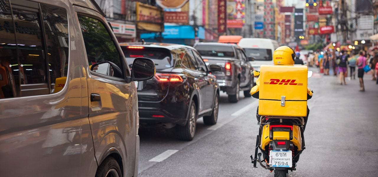 A male DHL driver on an electric motorcycle rides through the traffic in chinatown.