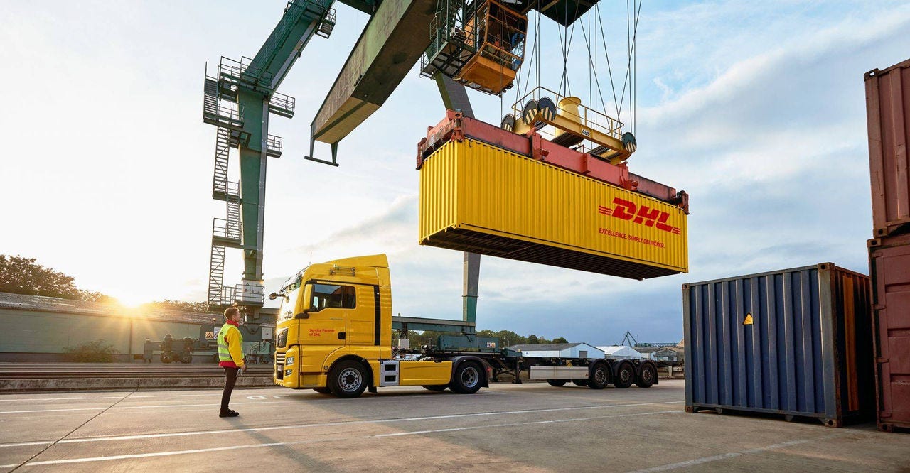a dhl employee standing in front of a dhl truck while watching a container crane lifting the container