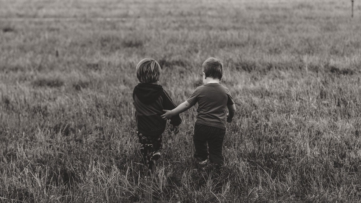 Black and white photo of the backs of two young boys walking in a field