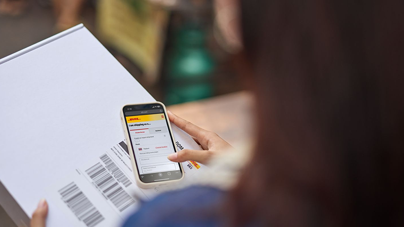 woman opening the dhl express app on her mobile phone with parcel in hand