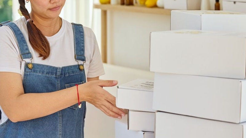 A young female shop employee is preparing white parcels for shipment. 