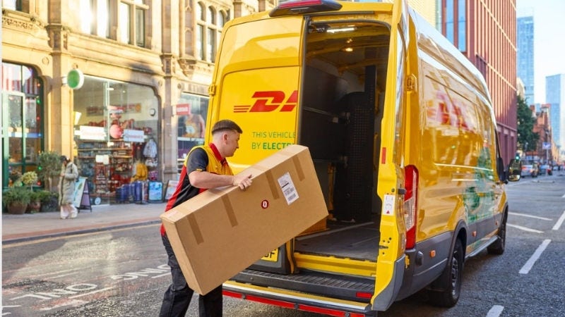 Inline Static ( 800x450)  - A male DHL employee loads a brown parcel into the cargo area of his electric DHL van.