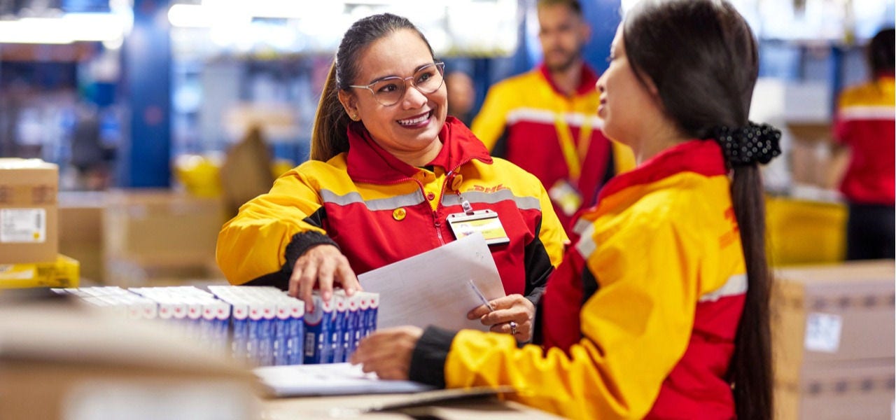 两名 DHL 仓库工作人员在仓储库区，对照单据核对货品，沟通作业信息。