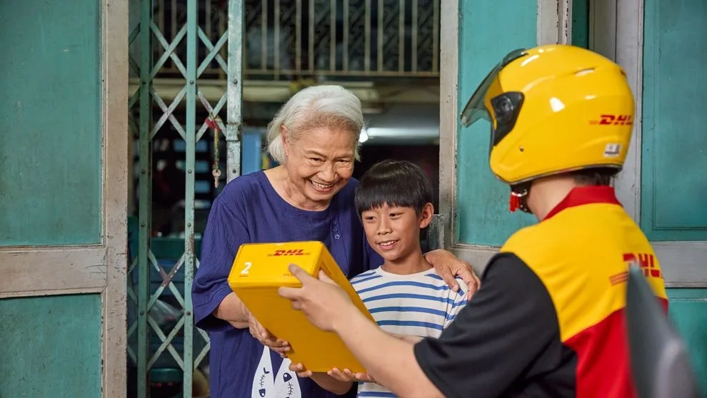 a grandmother and grandson receiving a parcel with japanese products from a dhl employee