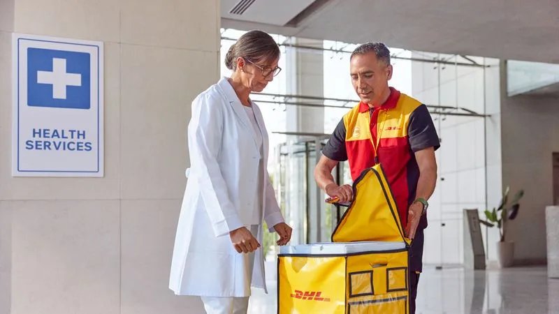 A DHL employee opens a yellow box of imported pharmaceutical products next to a female customer working in health services.