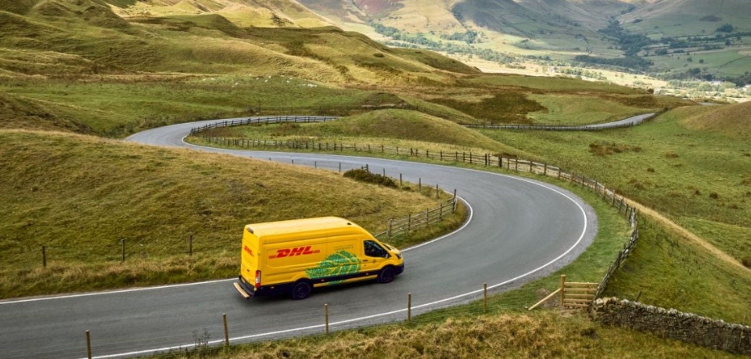 Header Banner( 1920x918)  - An electric DHL van drives on a winding road through a hill pass.