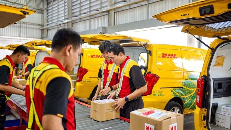 DHL Express staff sort and load parcels into yellow delivery vans inside a warehouse.