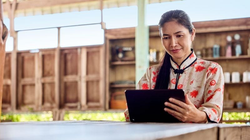 Seorang pemilik bisnis duduk di meja makan dan menggunakan tabletnya untuk mengajukan sertifikasi halal.