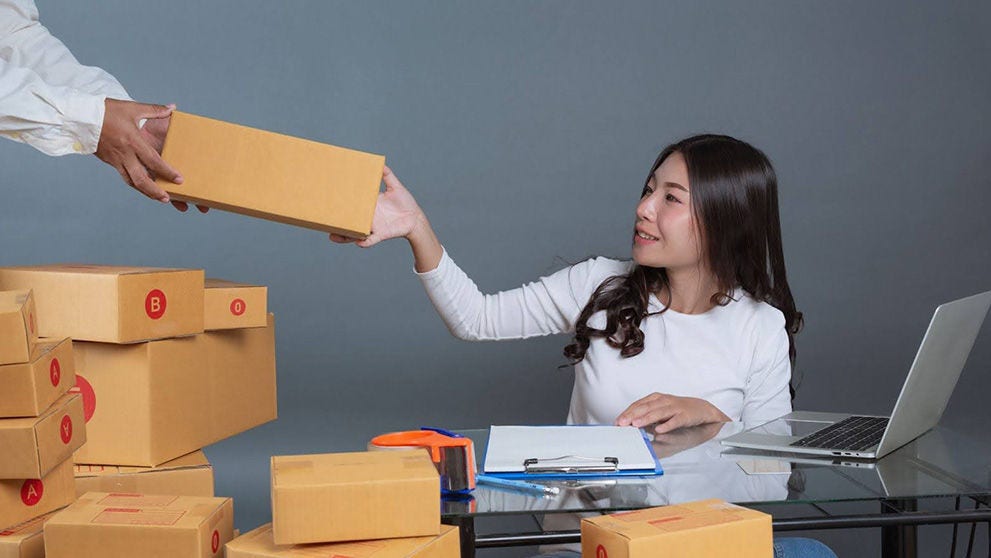 Seorang pengusaha wanita dengan laptop memberikan salah satu dari banyak paket kepada rekan kerja untuk bisnis dropship-nya