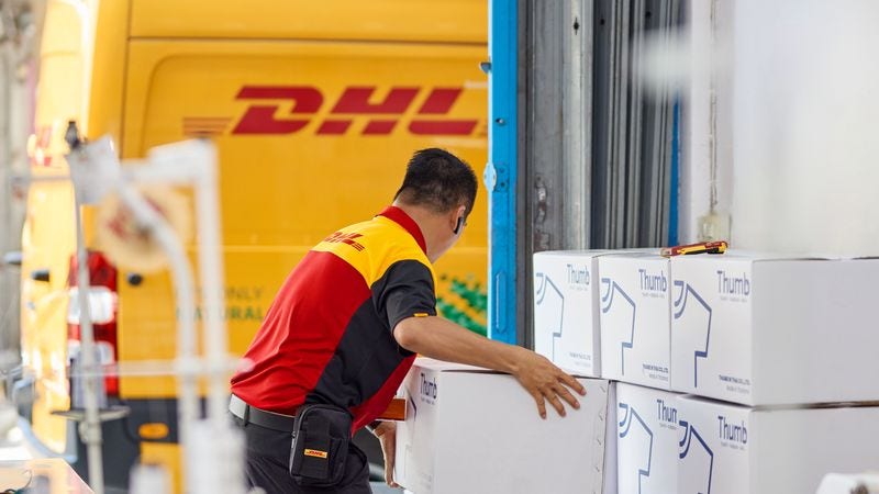 A DHL employee prepares to load boxes into a parked electric DHL van.