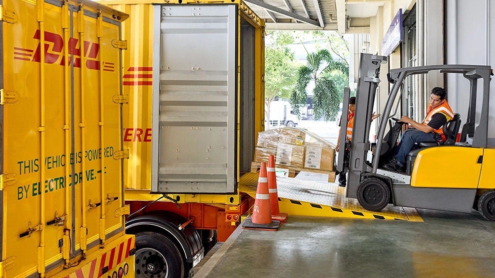 Empilhadeira carregando encomendas paletizadas em um caminhão da DHL