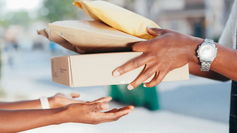 A person hands over a stack of three packages to another person.