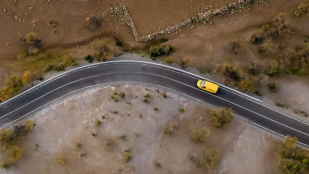 A DHL Express van making its way through a steppe landscape from a top-down view.