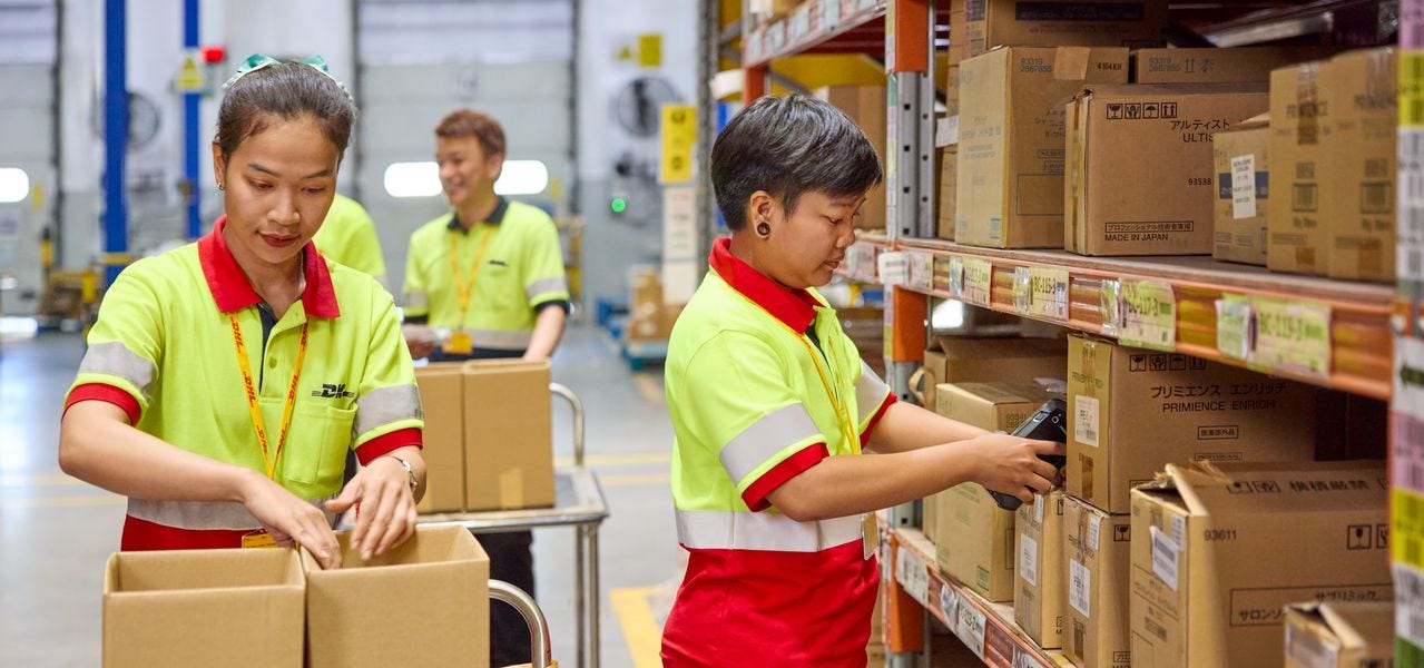 DHL employees picking and packing orders directly from a storage rack into a parcel at a multi-user warehouse.