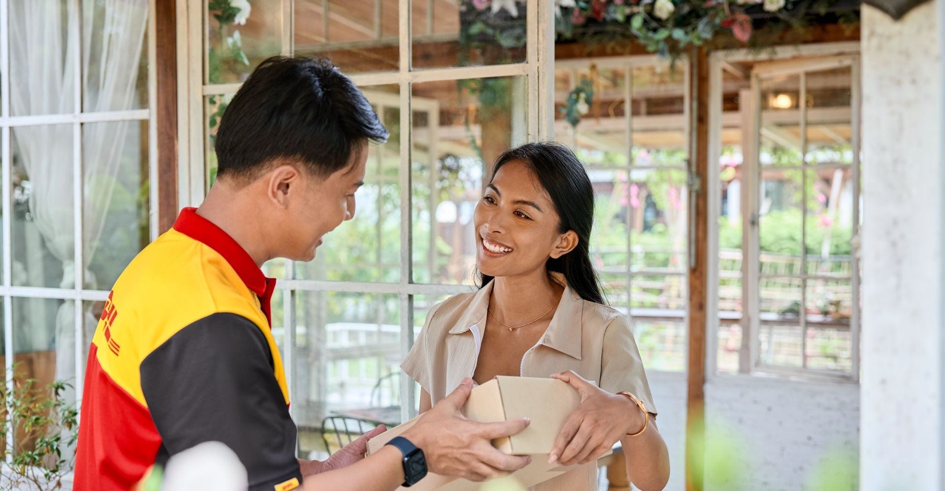 A male DHL employee hands over a parcel to a female customer in a remote house.