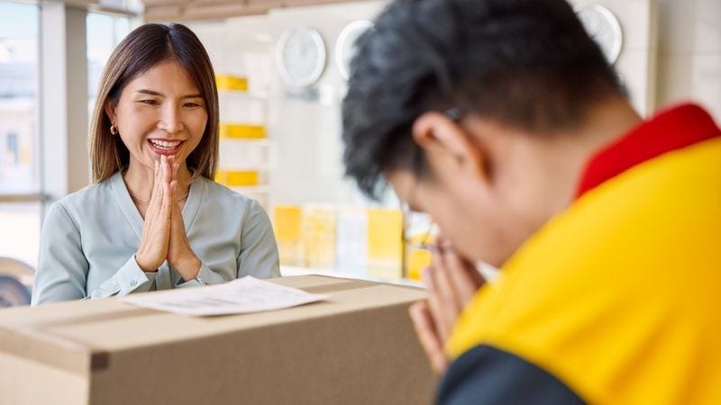 Female customer and DHL Express employee doing a traditional wai gesture as she drops off a package at a DHL Service Point