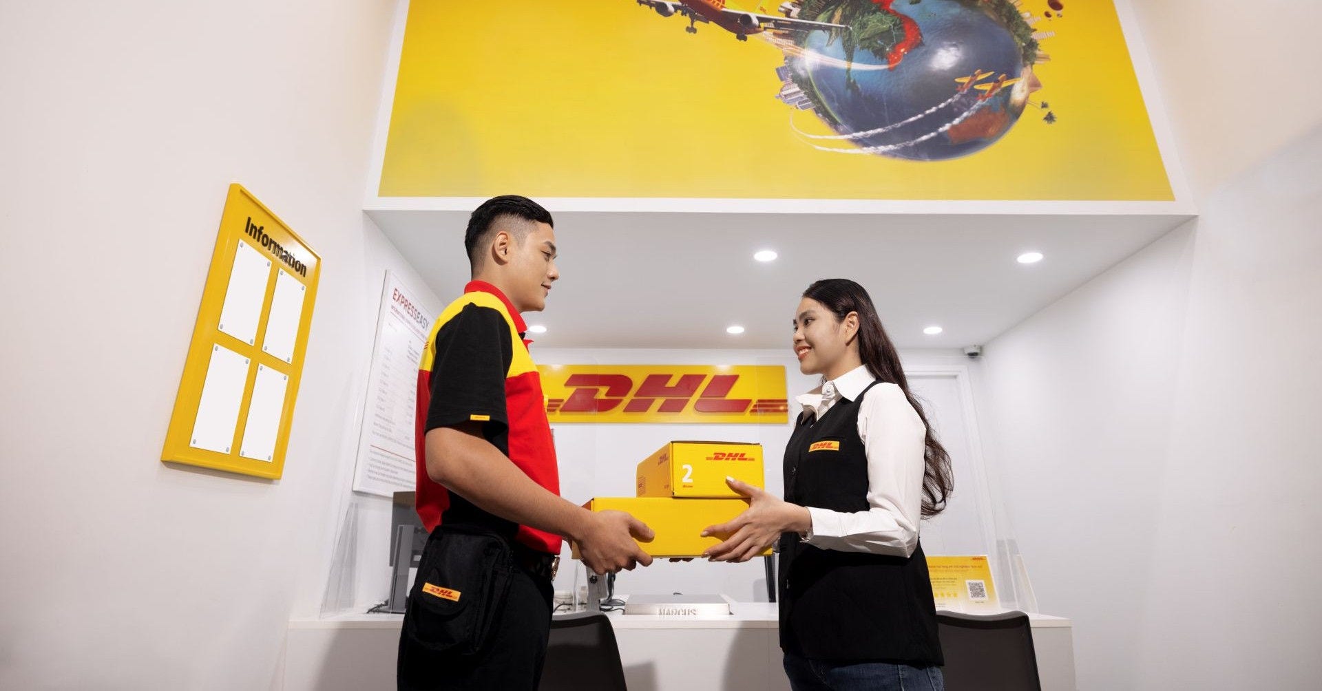 dhl employees exchanging a package at a service counter with a globe graphic