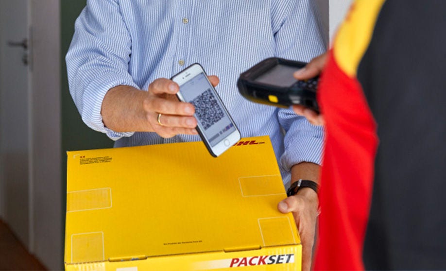 Man uses touchscreen at packstation holding smartphone and parcel