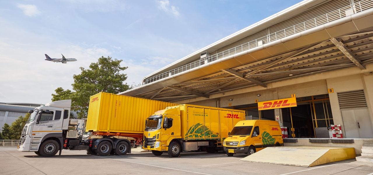 A DHL truck with trailer, an electric DHL truck and an electric DHL van parking at the loading bay of DGF Multimodal Hub.