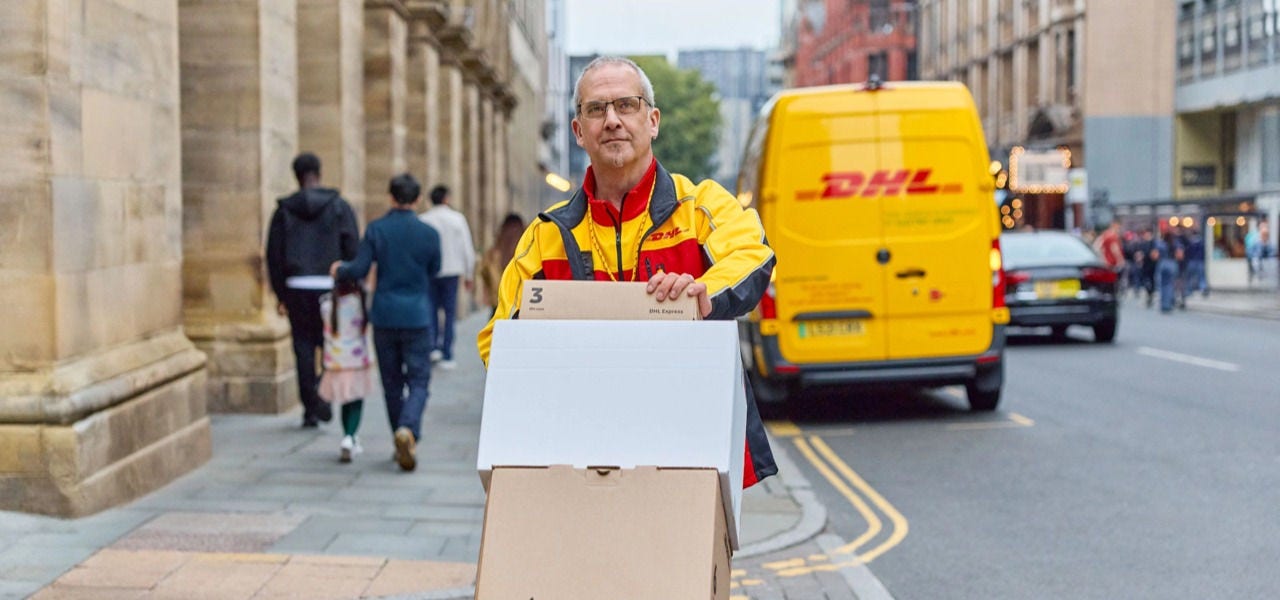 一名 DHL 员工推着装有若干包裹的手推车穿行街上