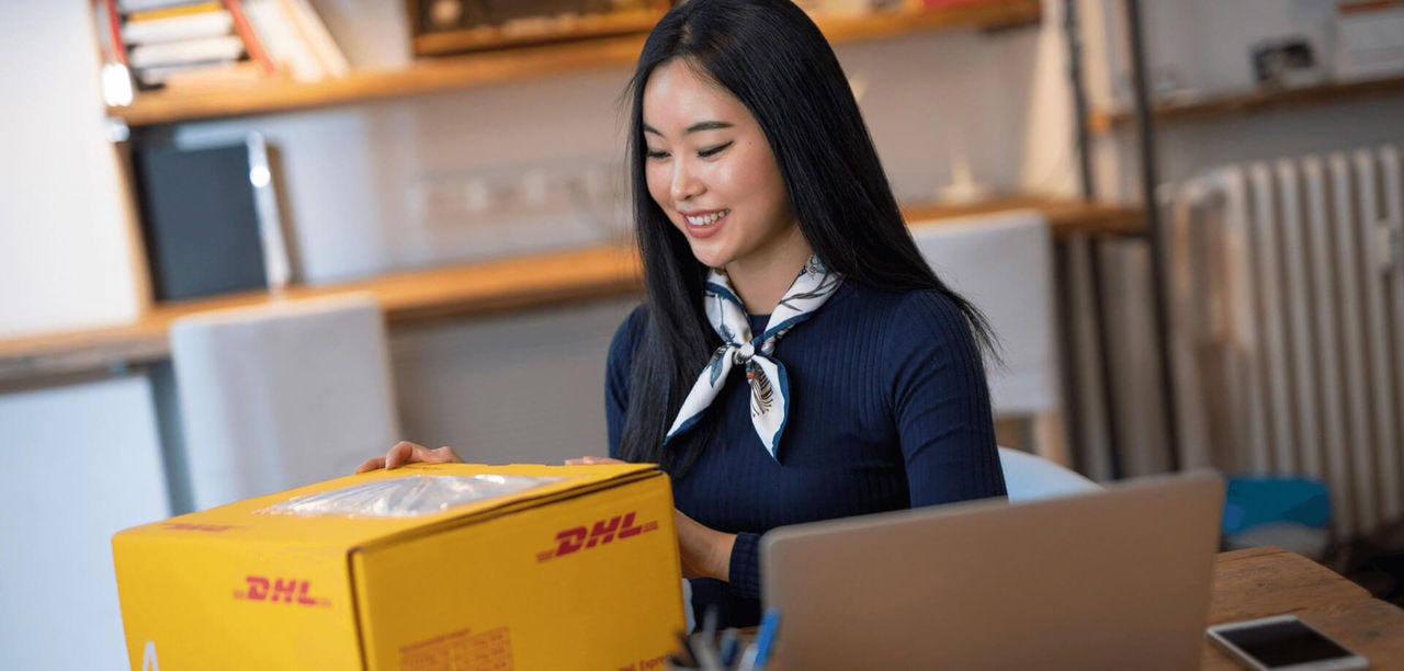 Woman placing shipping label onto a small business DHL package, preparing it to ship.