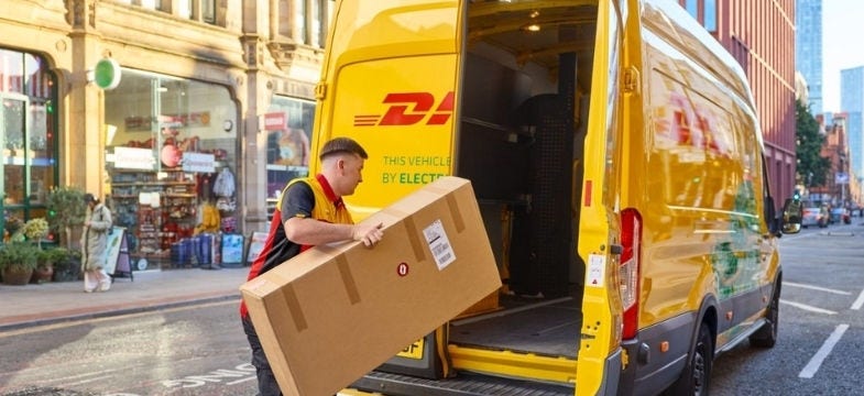 التشويش الخطي (800x450) - موظف ذكر في DHL يحمل طردا بنيا في منطقة الشحن في شاحنته الكهربائية DHL.