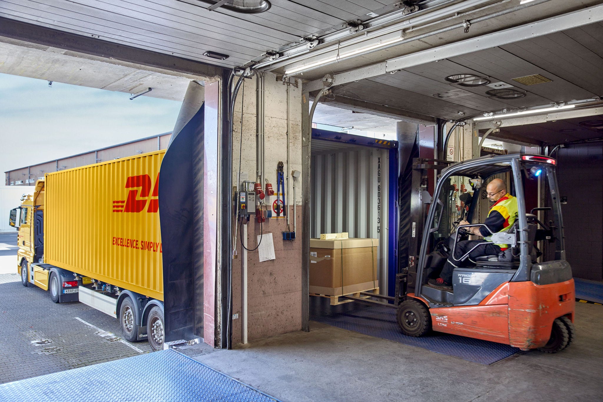 A male DHL employee is loading freight into a DHL truck with a forklift.