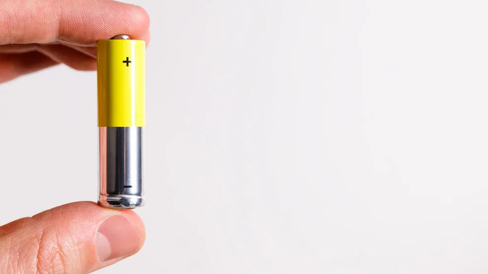 Man hand holding alkaline battery AA size, close up, isolated on white background with copy space. 