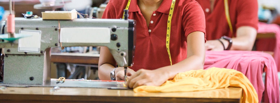 portrait of professional Seamstress in textile factory sewing with industrial sewing machine at garment