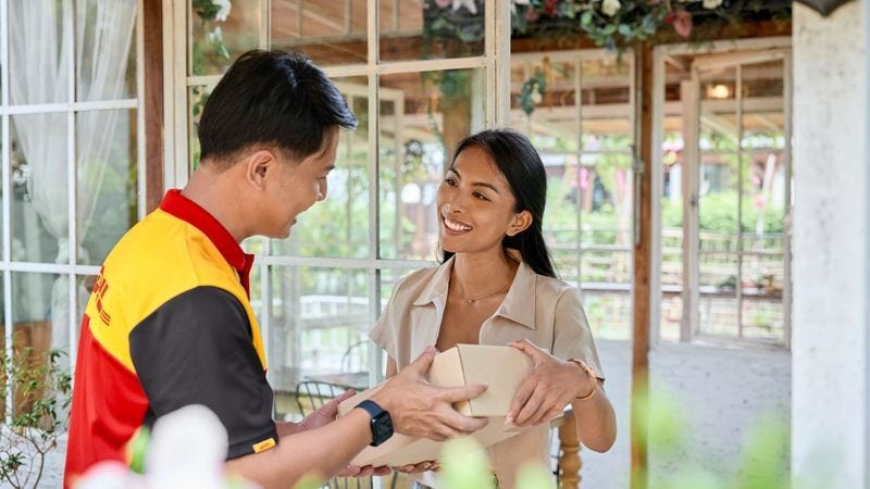 DHL courier handing a package to a smiling customer at her doorstep