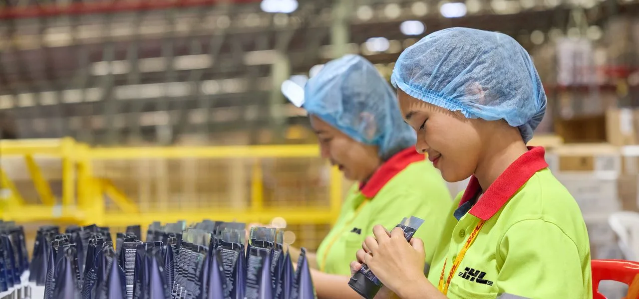 Female DHL employees relabeling products at a mezzanine in a multi-user warehouse