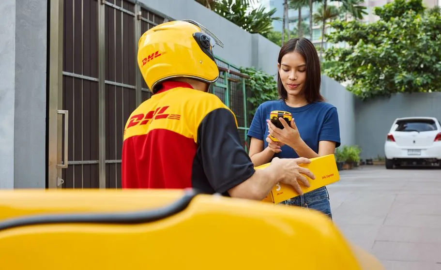 emale customer holding a scanner in her hand to sign while a male DHL employee is holding a parcel.