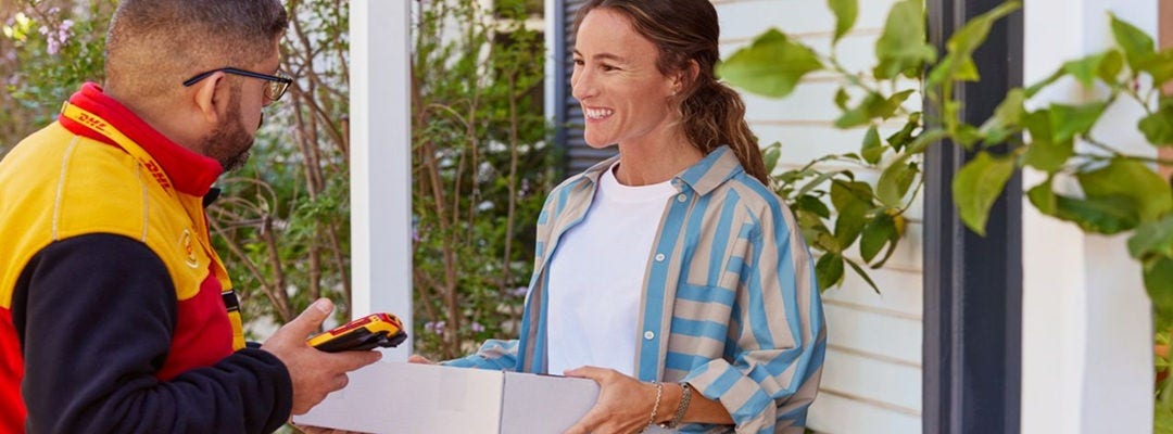 A male DHL employee is handing a white parcel to a female private customer at the door.
