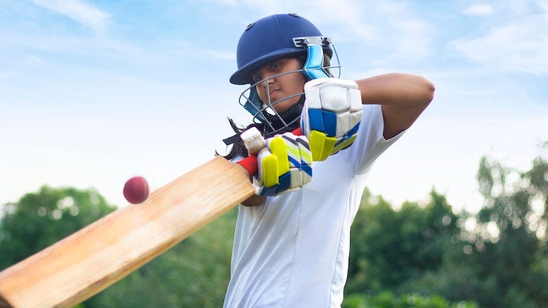 Indian Female cricket player wearing protective gear and hitting the ball with a bat on the field