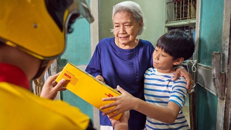 dhl employee handing a dhl express parcel to an elderly woman and a young boy at their front door