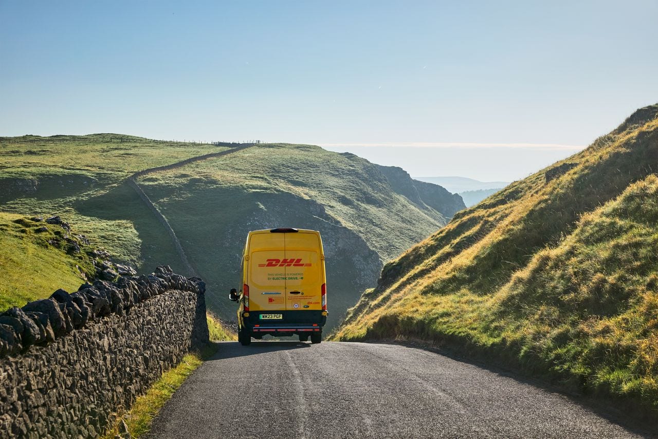 An electric DHL van drives through a hill pass. Back view and close up of the van.