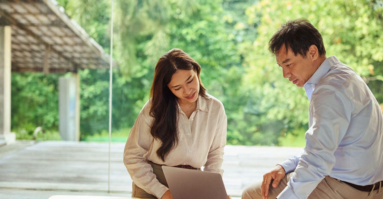 A male and female employee have a discussion at a table with a laptop between them