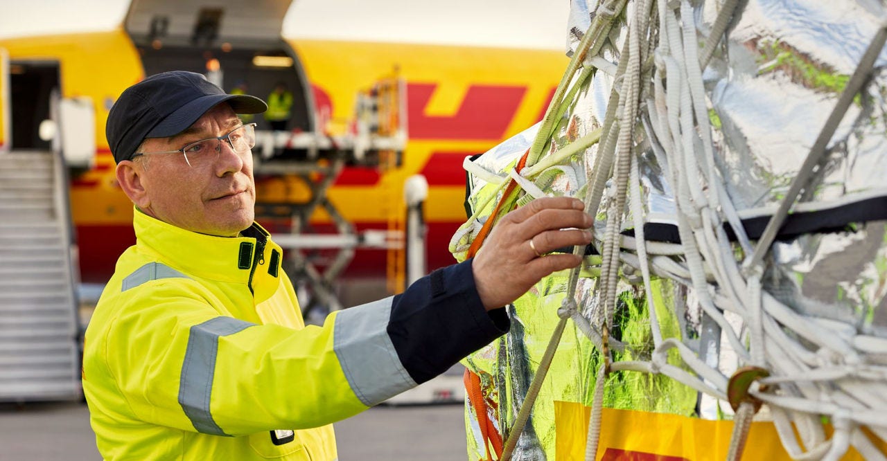 a dhl employee checking the security net of a shipment in front of an aeroplane in which the cargo will be loaded