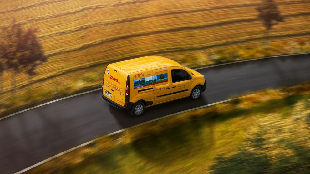 DHL Express van driving on road bordered by farmland