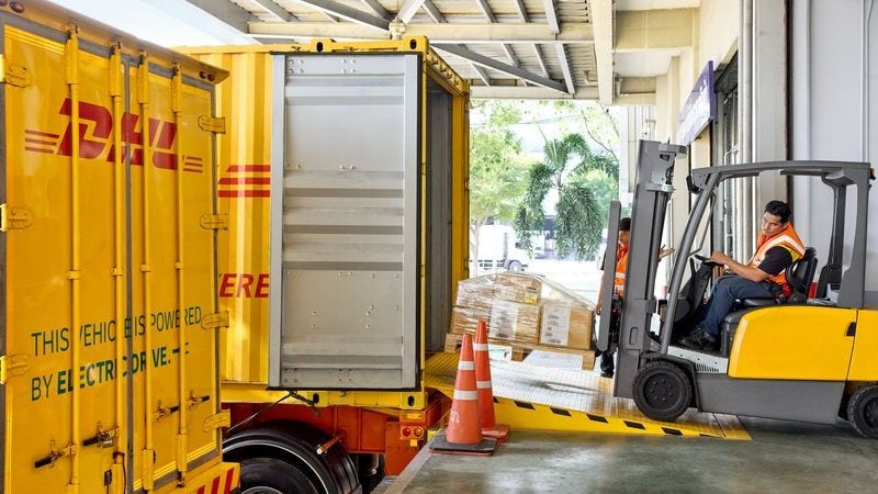 a dhl employee loading a pallet with a forklift into a shipping container