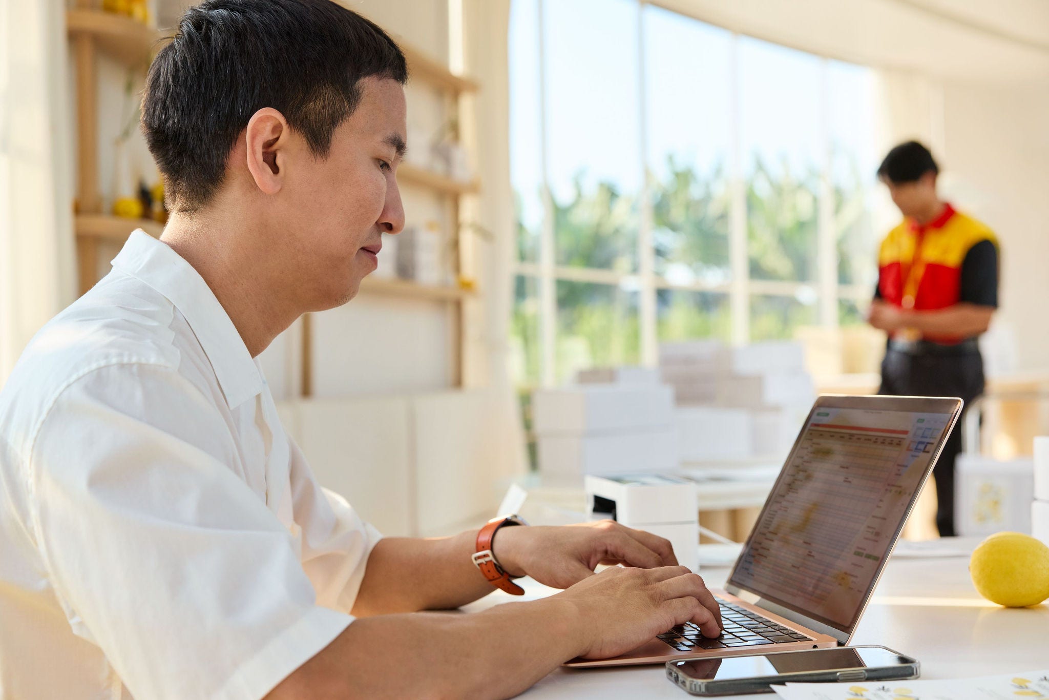 shop owner working at his desk while dhl employee takes care of a parcel pickup.