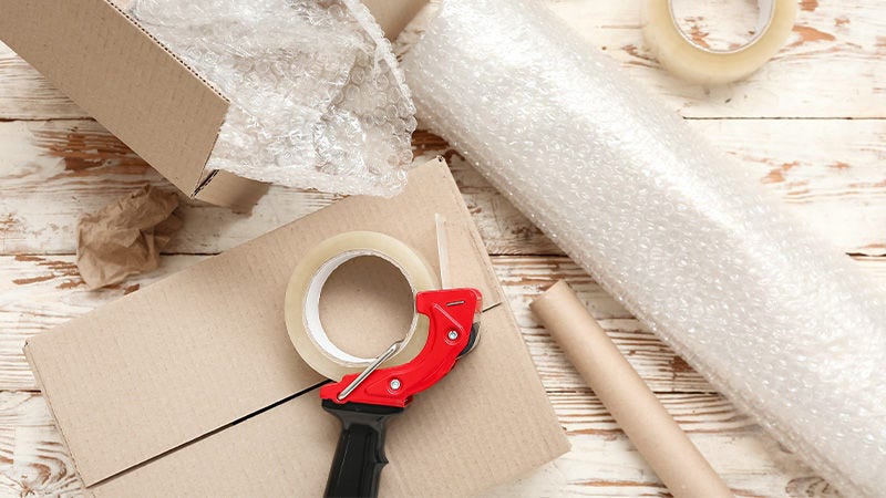 Packing tape dispenser, cardboard boxes and a roll of bubble wrap on a wooden table