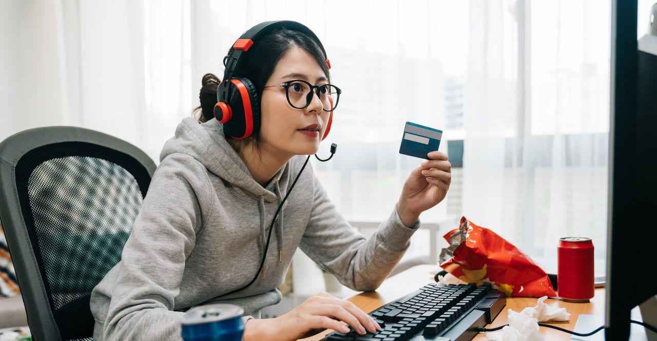 young lazy college girl nerd at home on summer break off from school holding credit card paying online e commerce buying game points. asian woman geek with headphones playing computer internet.