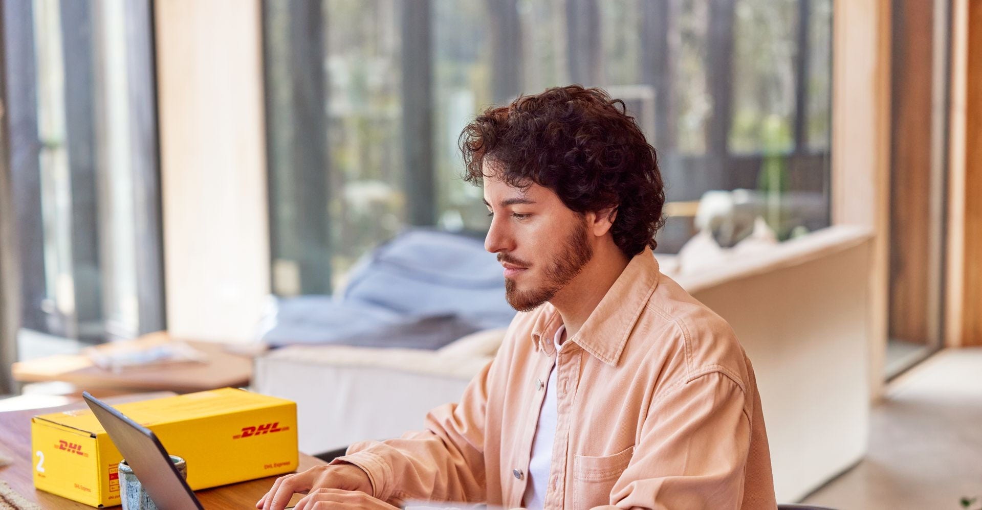 man using laptop with DHL parcel beside him 