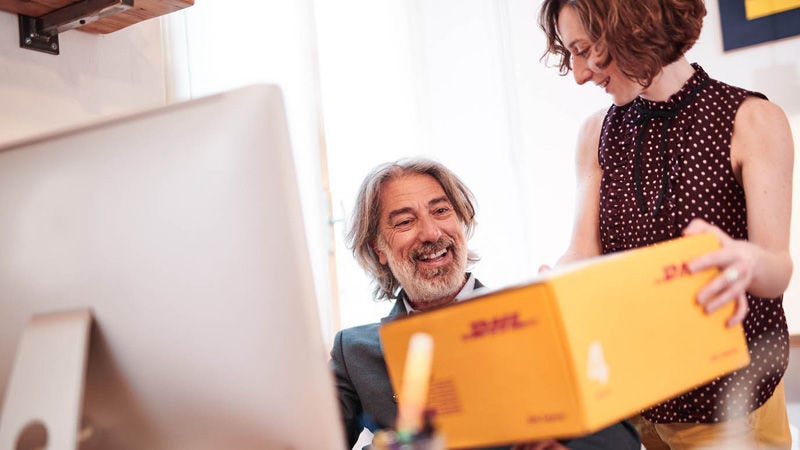 Kobieta wręcza mężczyźnie żółtą paczkę DHL