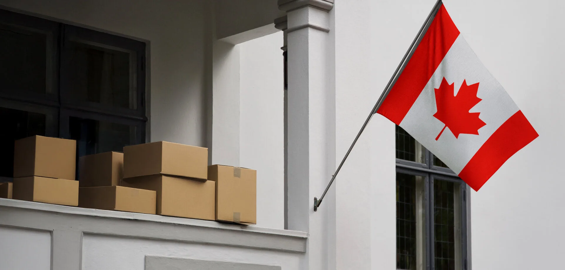 Canadian flag hanging from a flag post off the side of a building with shipping boxes stacked behind